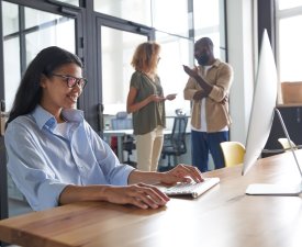 Woman working on computer in cozy office. Beautiful worker looking at screen with gladness and charming smile