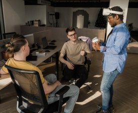 IT Development Team Working on VR Project. Man wearing VR headset, playing and touching something in the virtual world. Diverse men programmers using VR technologies and computer to create video game