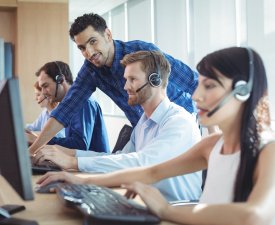 Smiling male supervisor assisting telemarketer at desk in call center